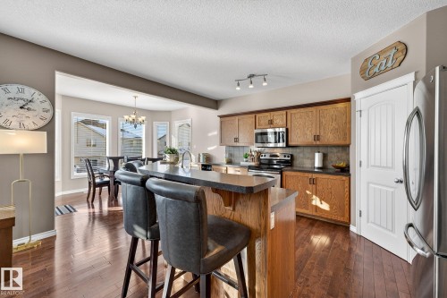 Kitchen featuring wood finish cabinets, dark countertops, stainless steel appliances, an island with sink, and dark wood-type flooring - 1734 63A Street, Edmonton, AB - Indoor
