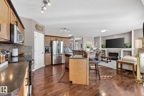 Kitchen with stainless steel appliances, a tile fireplace, an island with sink, a breakfast bar, and dark countertops - 1734 63A Street, Edmonton, AB - Indoor Photo Showing Kitchen With Fireplace With Stainless Steel Kitchen