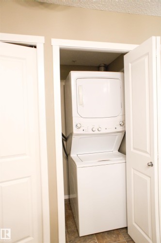 Laundry area featuring stacked washer and dryer and dark stone finish flooring - 104 5804 Place Nw, Edmonton, AB - Indoor Photo Showing Laundry Room