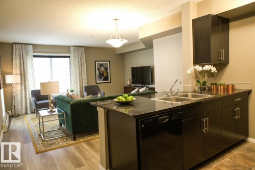 Kitchen featuring open floor plan, dishwasher, a peninsula, pendant lighting, and a textured ceiling - 104 5804 Place Nw, Edmonton, AB - Indoor Photo Showing Kitchen With Double Sink
