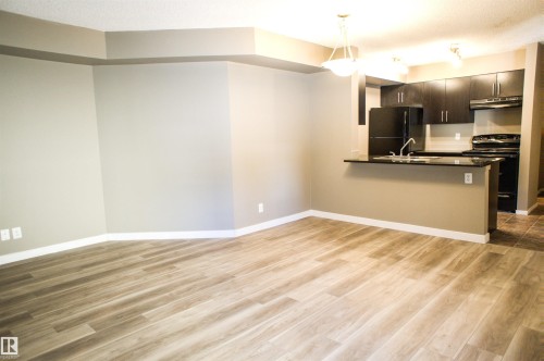 Kitchen with dark countertops, a peninsula, black appliances, decorative light fixtures, and dark wood finished floors - 104 5804 Place Nw, Edmonton, AB - Indoor Photo Showing Kitchen