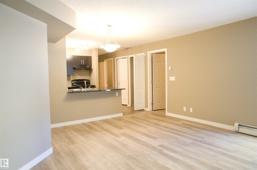Kitchen with a peninsula, light wood finished floors, pendant lighting, dark countertops, and electric range - 104 5804 Place Nw, Edmonton, AB - Indoor Photo Showing Other Room