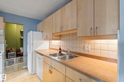 Kitchen with light wood finish cabinetry, light floors, white appliances, tasteful backsplash, and a textured ceiling - 