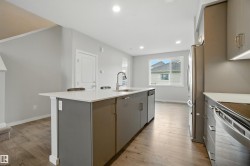 Kitchen with light wood-type flooring, recessed lighting, stainless steel appliances, gray cabinetry, and an island with sink - 