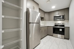 Kitchen with gray cabinetry, appliances with stainless steel finishes, light marble finish floors, decorative backsplash, and light countertops - 