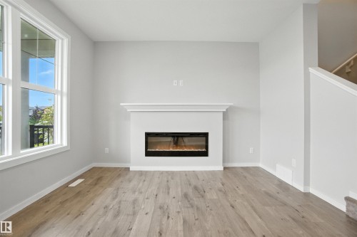 Unfurnished living room with a glass covered fireplace and light wood-style floors - 20727 25 Ave, Edmonton, AB - Indoor Photo Showing Living Room With Fireplace