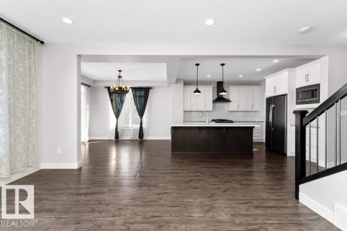 Kitchen with open floor plan, black refrigerator with ice dispenser, a kitchen island with sink, two tone color scheme, and stainless steel microwave - 62 Ellice Bend, Fort Saskatchewan, AB - Indoor Photo Showing Kitchen