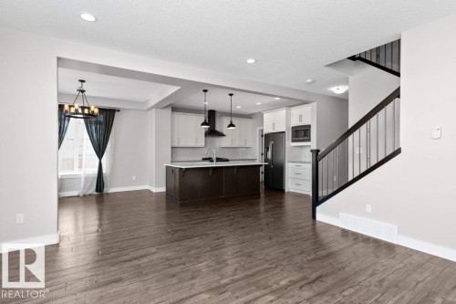 Two tone kitchen featuring two tone cabinets, light countertops, stainless steel fridge with ice dispenser, open floor plan, and a breakfast bar area - 62 Ellice Bend, Fort Saskatchewan, AB - Indoor