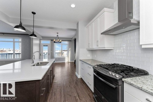 Two tone kitchen featuring range with gas stovetop, two tone color scheme, dark wood-style flooring, light stone countertops, and a chandelier - 62 Ellice Bend, Fort Saskatchewan, AB - Indoor Photo Showing Kitchen With Double Sink With Upgraded Kitchen
