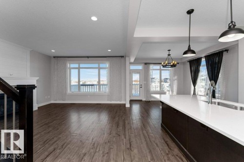Unfurnished living room with healthy amount of natural light, dark wood-type flooring, a textured ceiling, suspended lighting, and a large fireplace - 62 Ellice Bend, Fort Saskatchewan, AB - Indoor