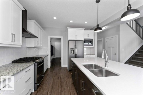 Kitchen featuring stainless steel appliances, hanging light fixtures, dark wood finished floors, light stone countertops, and a textured ceiling - 62 Ellice Bend, Fort Saskatchewan, AB - Indoor Photo Showing Kitchen With Double Sink With Upgraded Kitchen