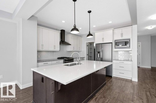 Kitchen featuring dual tone cabinets, an island with sink, a kitchen bar, dark wood-type flooring, and hanging light fixtures - 62 Ellice Bend, Fort Saskatchewan, AB - Indoor Photo Showing Kitchen With Double Sink With Upgraded Kitchen