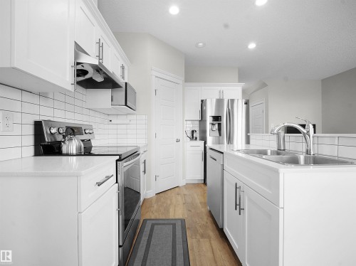 Kitchen featuring stainless steel appliances, tasteful backsplash, ventilation hood, light wood-style floors, and white cabinetry - 218 Hawks Ridge Boulevard, Edmonton, AB - Indoor Photo Showing Kitchen With Double Sink With Upgraded Kitchen