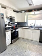 Kitchen featuring appliances with stainless steel finishes, a textured ceiling, dark countertops, white cabinets, and under cabinet range hood - 
