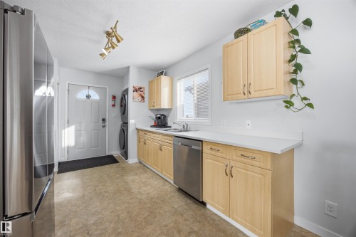 Kitchen featuring stainless steel appliances, light countertops, light wood finish cabinets, stacked washer / drying machine, and a textured ceiling - 2340 30 Avenue, Edmonton, AB - Indoor Photo Showing Kitchen