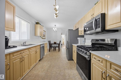 Kitchen featuring stainless steel appliances, light countertops, light wood finish cabinets, suspended lighting, and a textured ceiling - 2340 30 Avenue, Edmonton, AB - Indoor Photo Showing Kitchen With Double Sink