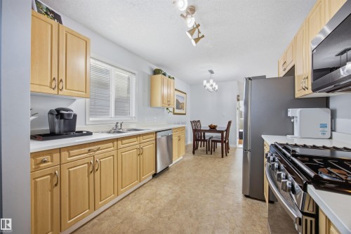 Kitchen with light countertops, stainless steel appliances, light wood finish cabinetry, a textured ceiling, and hanging lights - 2340 30 Avenue, Edmonton, AB - Indoor Photo Showing Kitchen With Double Sink