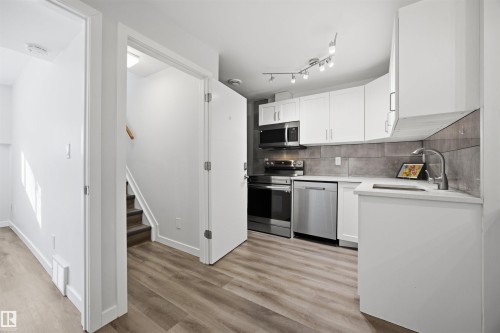 Kitchen featuring white cabinets, stainless steel appliances, light wood finished floors, light stone countertops, and tasteful backsplash - 2340 30 Avenue, Edmonton, AB - Indoor Photo Showing Kitchen