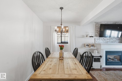 Dining space with a textured ceiling, a glass covered fireplace, a chandelier, radiator, and dark wood-style floors - 18717 57 Avenue, Edmonton, AB - Indoor Photo Showing Dining Room With Fireplace
