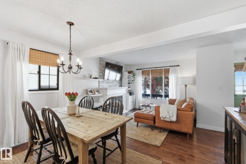Dining space featuring dark wood-style floors, suspended lighting, a fireplace, and a textured ceiling - 18717 57 Avenue, Edmonton, AB - Indoor Photo Showing Dining Room