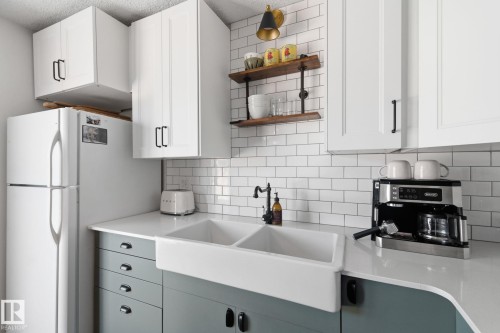 Kitchen featuring freestanding refrigerator, open shelves, two tone cabinets, tasteful backsplash, and light stone counters - 18717 57 Avenue, Edmonton, AB - Indoor Photo Showing Kitchen With Double Sink