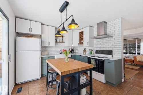 Dual tone kitchen featuring range with electric stovetop, hanging light fixtures, freestanding refrigerator, two tone cabinets, and plenty of natural light - 18717 57 Avenue, Edmonton, AB - Indoor Photo Showing Kitchen