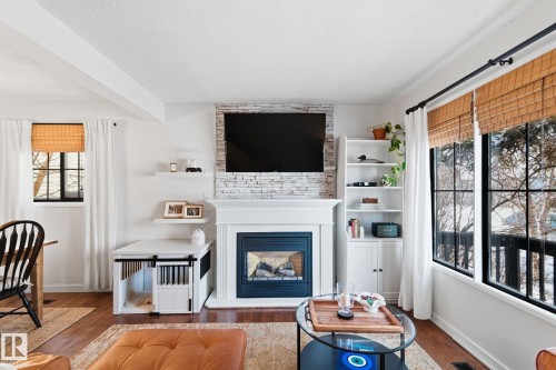 Living area with a large fireplace, wood finished floors, and a textured ceiling - 18717 57 Avenue, Edmonton, AB - Indoor Photo Showing Living Room With Fireplace