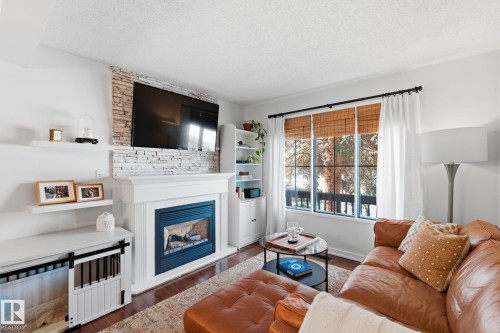 Living area with a glass covered fireplace, a textured ceiling, and wood finished floors - 18717 57 Avenue, Edmonton, AB - Indoor Photo Showing Living Room With Fireplace