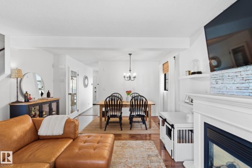 Living area with dark wood-style floors, a glass covered fireplace, suspended lighting, and plenty of natural light - 18717 57 Avenue, Edmonton, AB - Indoor Photo Showing Living Room With Fireplace
