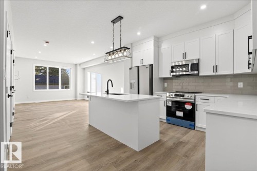 Kitchen with stainless steel appliances, a center island with sink, pendant lighting, tasteful backsplash, and light wood-type flooring - 10506 162 Street, Edmonton, AB - Indoor Photo Showing Kitchen With Upgraded Kitchen