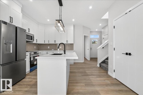 Kitchen featuring stainless steel appliances, an island with sink, light wood-style floors, and white cabinets - 10506 162 Street, Edmonton, AB - Indoor Photo Showing Kitchen