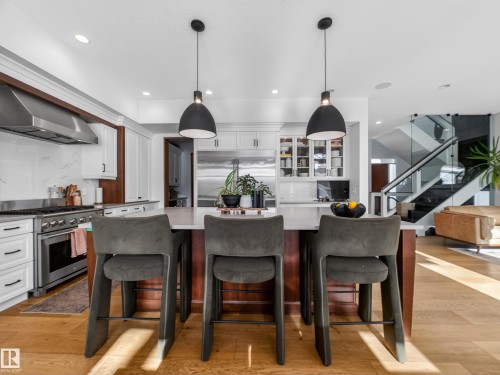 Dual tone kitchen with ventilation hood, high quality appliances, light wood-type flooring, pendant lighting, and glass fronted cabinets - 5507 Chegwin Point(E), Edmonton, AB - Indoor Photo Showing Other Room