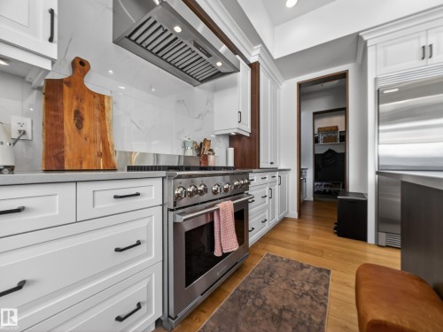 Kitchen featuring white cabinets, high end appliances, extractor fan, light wood-style floors, and dark stone countertops - 5507 Chegwin Point(E), Edmonton, AB - Indoor Photo Showing Kitchen With Upgraded Kitchen