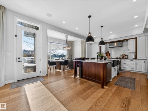 Two tone kitchen featuring dual tone cabinetry, a kitchen island with sink, pendant lighting, light wood-style floors, and a kitchen bar - 5507 Chegwin Point(E), Edmonton, AB - Indoor Photo Showing Kitchen With Upgraded Kitchen