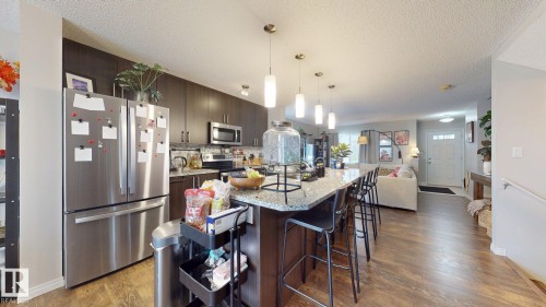 Kitchen with stainless steel appliances, dark wood finish cabinets, a kitchen island with sink, a kitchen breakfast bar, and light stone counters - 1275 Chappelle Boulevard Sw, Edmonton, AB - Indoor Photo Showing Kitchen With Upgraded Kitchen