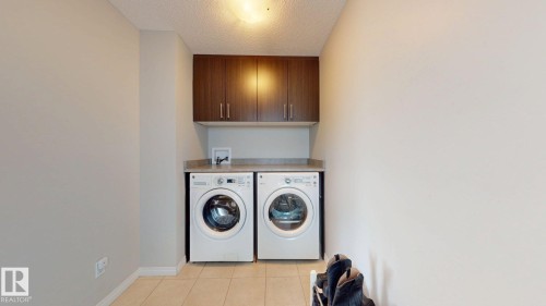 Laundry area with a textured ceiling, cabinet space, washer and dryer, and light tile patterned floors - 1275 Chappelle Boulevard Sw, Edmonton, AB - Indoor Photo Showing Laundry Room