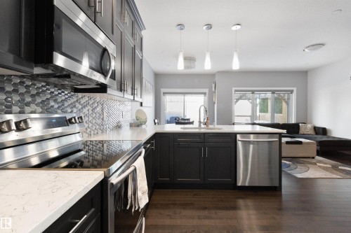 Kitchen with stainless steel appliances, open floor plan, decorative backsplash, dark wood-type flooring, and pendant lighting - 56 Durrand Bend, Fort Saskatchewan, AB - Indoor Photo Showing Kitchen With Upgraded Kitchen