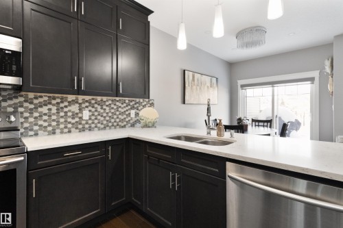 Kitchen featuring stainless steel appliances, light stone counters, pendant lighting, backsplash, and dark cabinetry - 56 Durrand Bend, Fort Saskatchewan, AB - Indoor Photo Showing Kitchen With Double Sink With Upgraded Kitchen