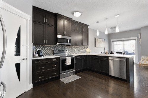 Kitchen featuring stainless steel appliances, decorative light fixtures, dark wood finished floors, a peninsula, and light stone countertops - 56 Durrand Bend, Fort Saskatchewan, AB - Indoor Photo Showing Kitchen With Upgraded Kitchen
