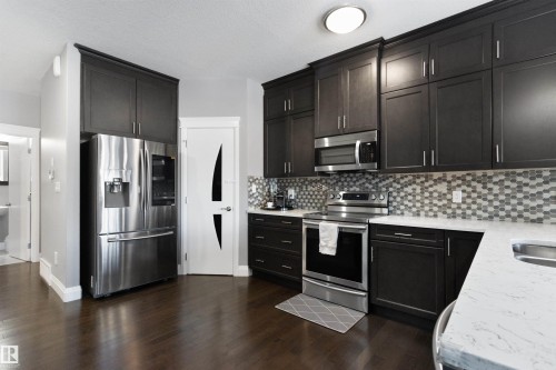 Kitchen featuring stainless steel appliances, light stone countertops, dark wood finished floors, and decorative backsplash - 56 Durrand Bend, Fort Saskatchewan, AB - Indoor Photo Showing Kitchen With Double Sink With Upgraded Kitchen