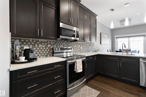 Kitchen featuring stainless steel appliances, dark wood-style floors, pendant lighting, light stone counters, and backsplash - 56 Durrand Bend, Fort Saskatchewan, AB - Indoor Photo Showing Kitchen With Upgraded Kitchen
