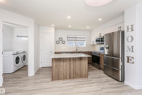 Dual tone kitchen with a kitchen island, stainless steel appliances, light countertops, a textured ceiling, and backsplash - 2412 192 Street, Edmonton, AB - Indoor Photo Showing Laundry Room