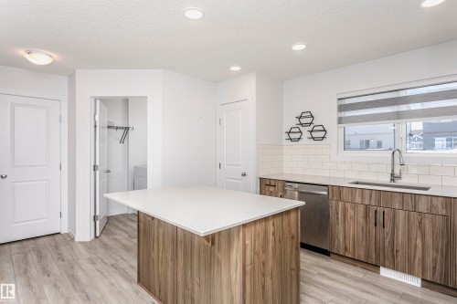 Kitchen with wood finish cabinetry, a kitchen island, decorative backsplash, stainless steel dishwasher, and a textured ceiling - 2412 192 Street, Edmonton, AB - Indoor Photo Showing Kitchen
