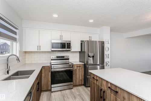 Kitchen with stainless steel appliances, light stone counters, dual tone cabinetry, light wood-style floors, and a textured ceiling - 2412 192 Street, Edmonton, AB - Indoor Photo Showing Kitchen With Stainless Steel Kitchen With Double Sink With Upgraded Kitchen