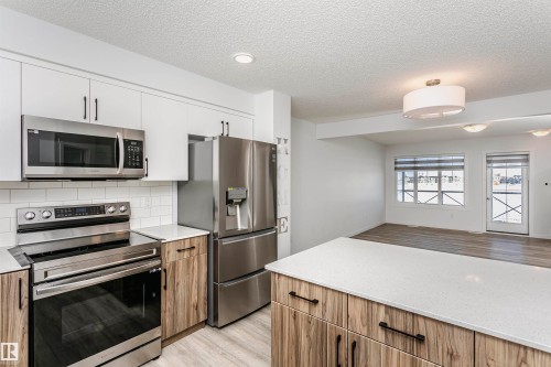 Kitchen with stainless steel appliances, light stone countertops, light wood-style flooring, open floor plan, and a textured ceiling - 2412 192 Street, Edmonton, AB - Indoor Photo Showing Kitchen With Stainless Steel Kitchen With Upgraded Kitchen
