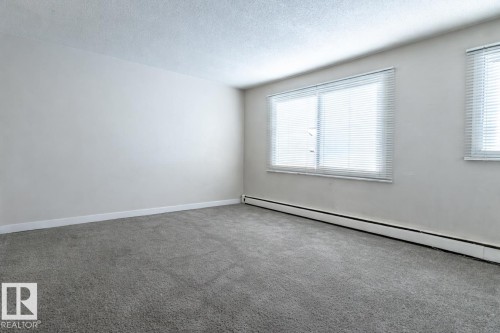 Carpeted empty room featuring baseboard heating and a textured ceiling - 15 10620 122 Street, Edmonton, AB - Indoor Photo Showing Other Room