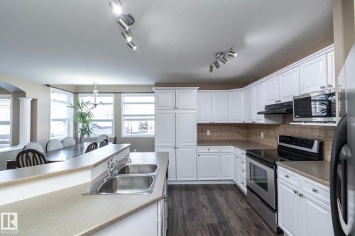 Kitchen featuring stainless steel appliances, white cabinets, backsplash, dark wood-style flooring, and rail lighting - 16454 61A Street, Edmonton, AB - Indoor Photo Showing Kitchen With Double Sink