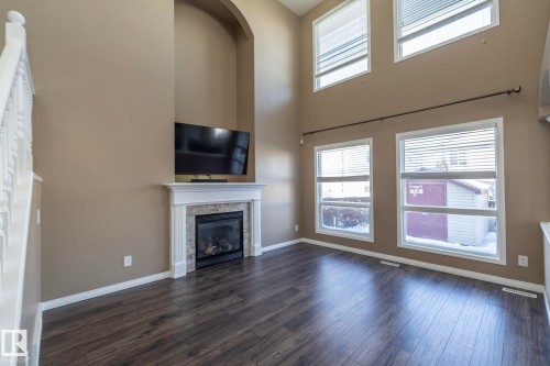 Unfurnished living room with plenty of natural light, a glass covered fireplace, dark wood finished floors, and a high ceiling - 16454 61A Street, Edmonton, AB - Indoor Photo Showing Living Room With Fireplace