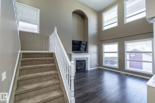 Staircase featuring a glass covered fireplace, wood finished floors, and a high ceiling - 16454 61A Street, Edmonton, AB - Indoor With Fireplace