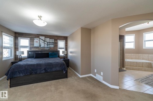 Carpeted bedroom with arched walkways, tile patterned flooring, a textured ceiling, and wooden walls - 16454 61A Street, Edmonton, AB - Indoor Photo Showing Bedroom